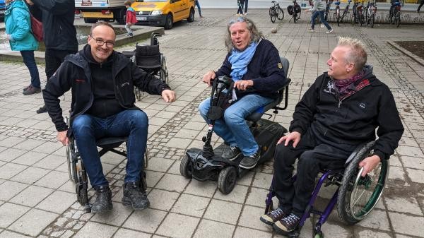 Drei Männer sitzen in Rollstühlen